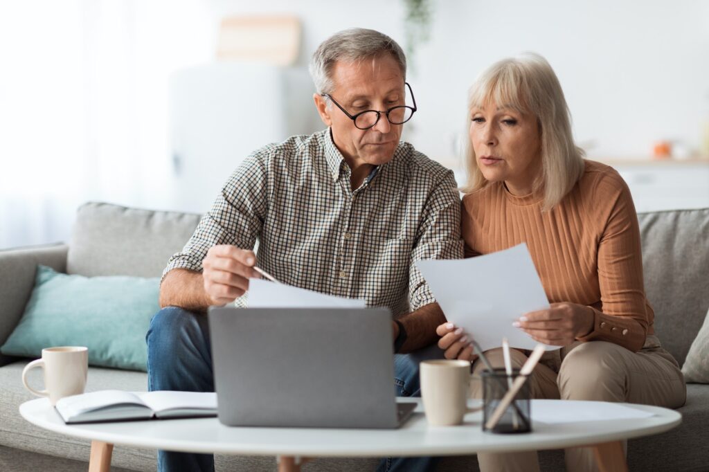 Senior Couple Looking Through Papers Counting Reading Bills At Home